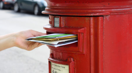 girls hand posting letters to red british postbox on street