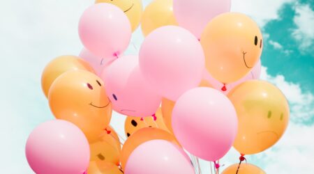 A bouquet of balloons pink and orange with faces drawn on.