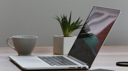 Open laptop surrounded by a phone, a mug, and a small plant