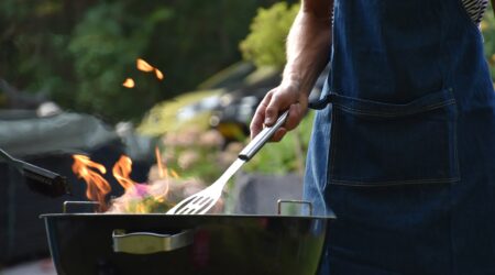 Someone wearing a denim apron and flipping burgers on a barbeque