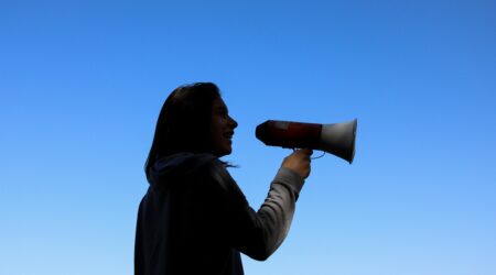 A woman speaking into a megaphone with a blue sky behind her.
