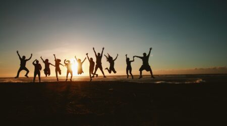 A group of people jumping on a hill silhouetted by the sunset.
