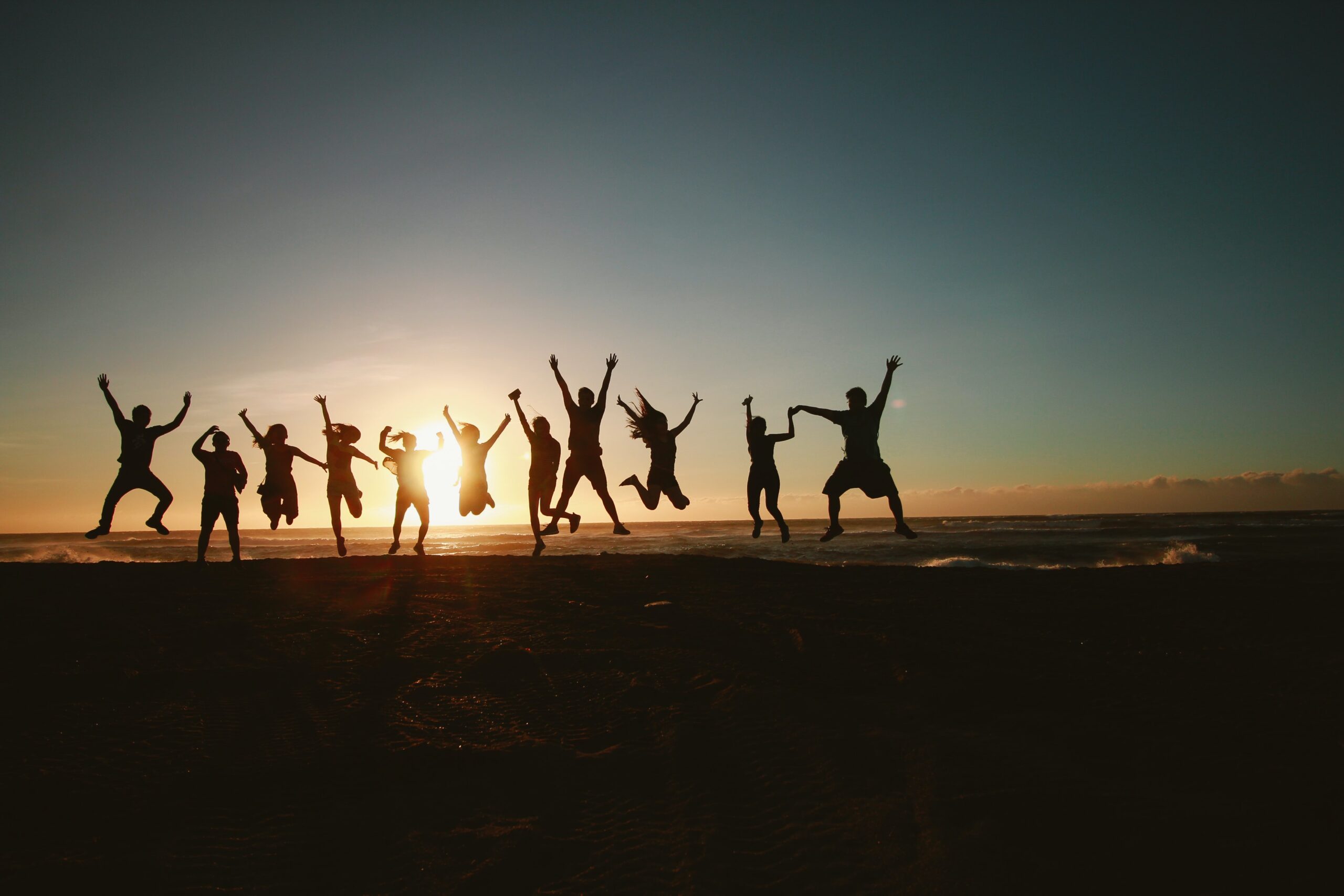 A group of people jumping on a hill silhouetted by the sunset.