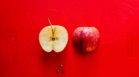 A halved apple on a red background. One half is on the right and laying face down and the other is laying face up exposing the core.