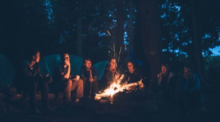 A group of people sit and chat around a campfire.